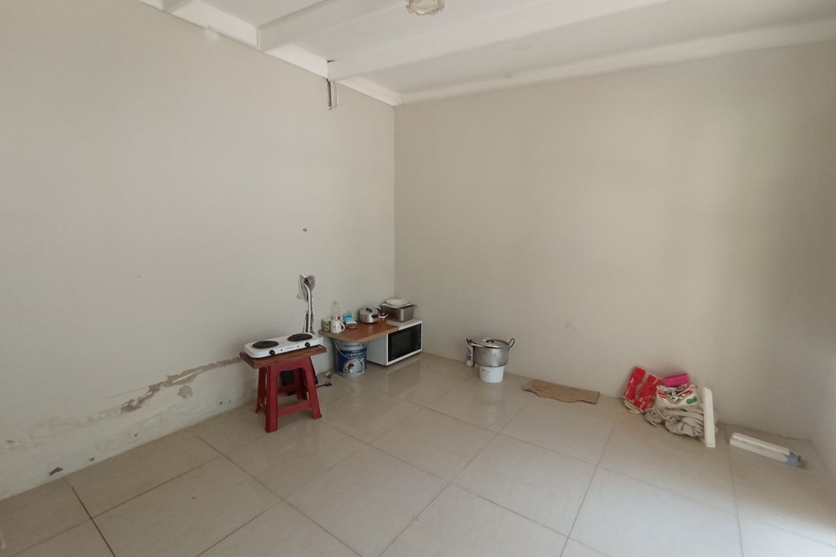 A basic, empty kitchen area featuring tiled flooring and exposed ceiling beams, currently requiring maintenance and cosmetic updates to the wall finishes.