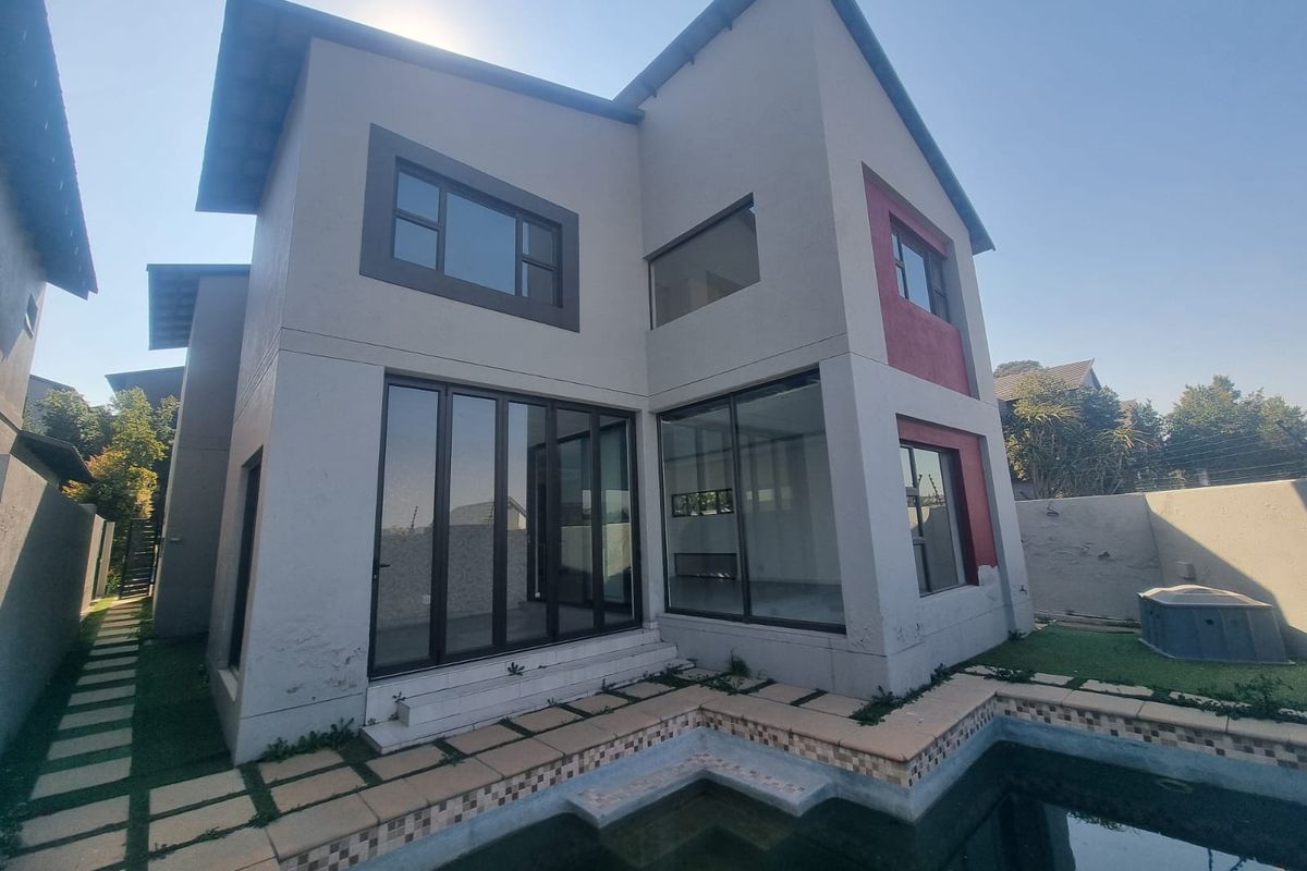 Rear exterior view of a two-story house featuring a swimming pool, tiled patio area, and large sliding glass doors.
