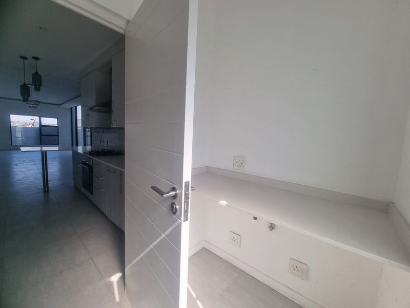A clean, modern scullery or utility area featuring built-in cabinetry, stone countertops, and tiled flooring, adjacent to the main kitchen space.