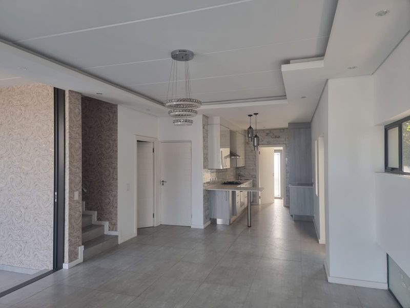 Spacious open-plan living area featuring modern tiled floors, a contemporary kitchen with built-in appliances, and elegant feature wallpaper.