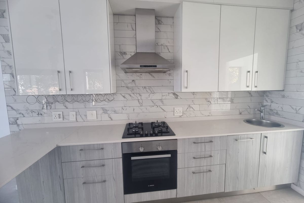 Modern kitchen featuring white and wood-grain cabinetry, quartz countertops, marble-look backsplash, and integrated stainless steel appliances including a gas hob and oven.
