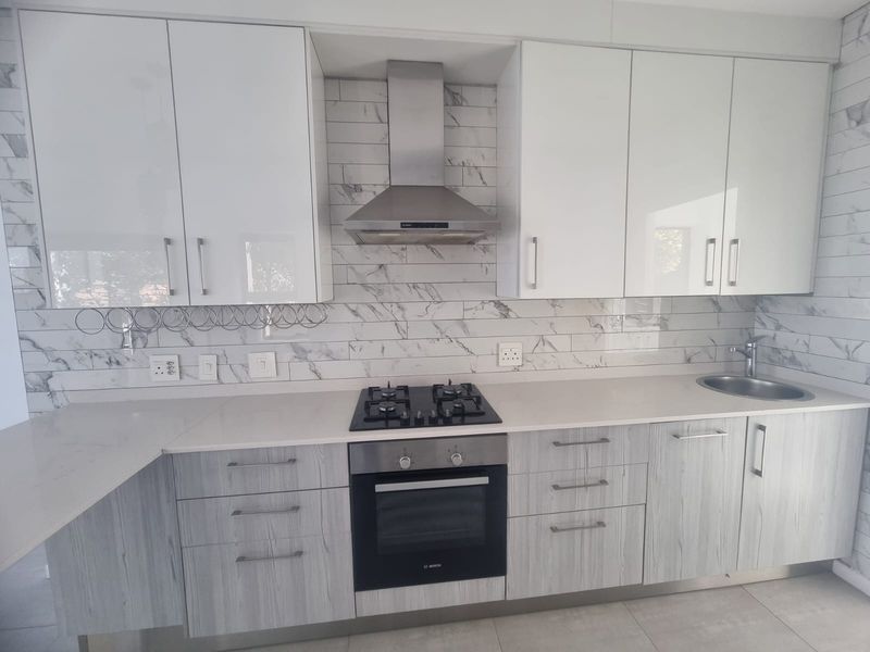 Modern kitchen featuring white and wood-grain cabinetry, quartz countertops, marble-look backsplash, and integrated stainless steel appliances including a gas hob and oven.