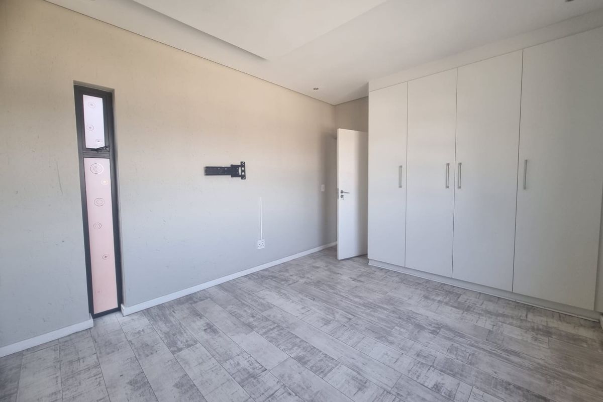 A clean, modern bedroom featuring neutral walls, wood-look tiled flooring, and ample built-in cupboard storage.