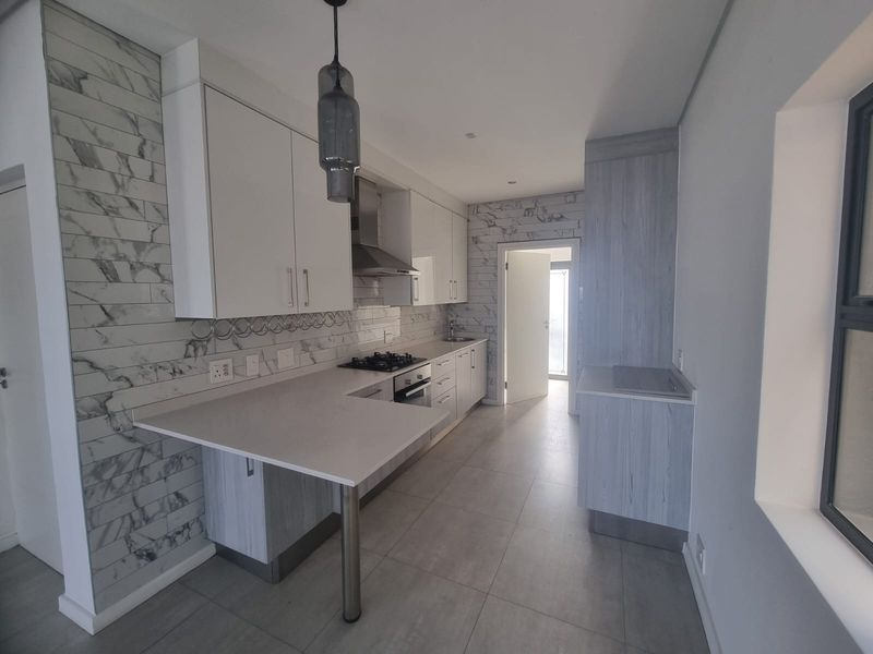 Modern kitchen featuring sleek white cabinetry, stone countertops, marble-effect backsplash, and integrated appliances in a clean, contemporary layout.