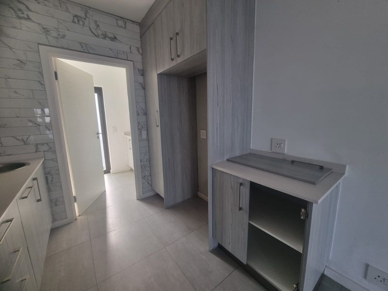 A modern, empty scullery featuring light wood-grain cabinetry, marble-effect wall tiles, and neutral floor tiles, providing functional prep and storage space.