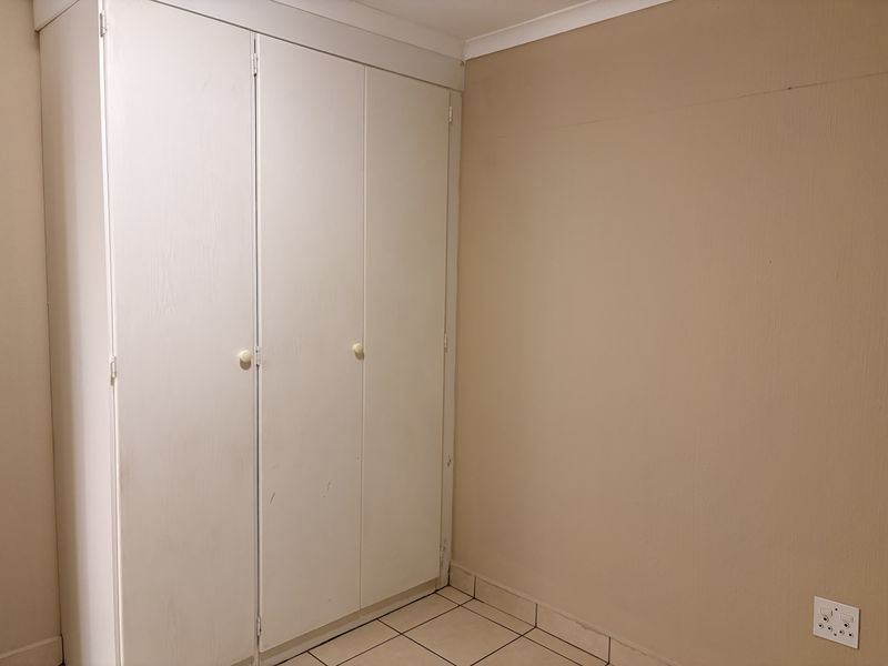 A simple bedroom featuring tiled flooring and a white built-in wardrobe with three doors.