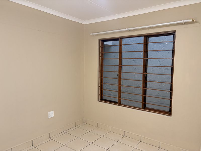 A clean, empty bedroom featuring neutral wall paint, tiled flooring, and a window fitted with security bars.