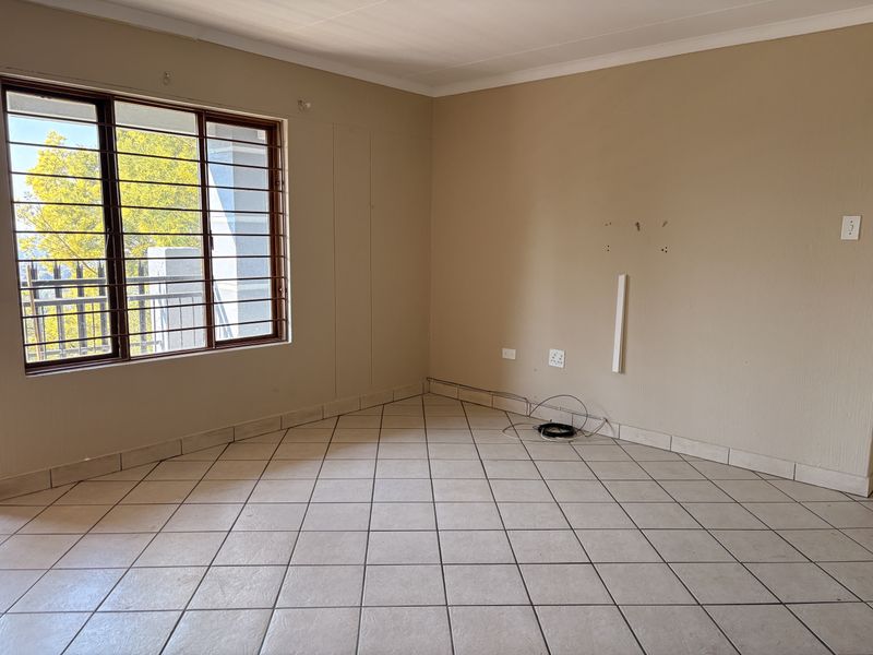 An empty living room featuring tiled flooring, security bars on the window, and neutral wall finishes, ready for personalization.