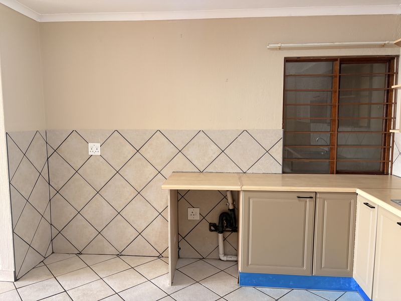 A functional kitchen area featuring tiled splashbacks, laminate countertops, and built-in cabinetry with dedicated plumbing connections for appliances.