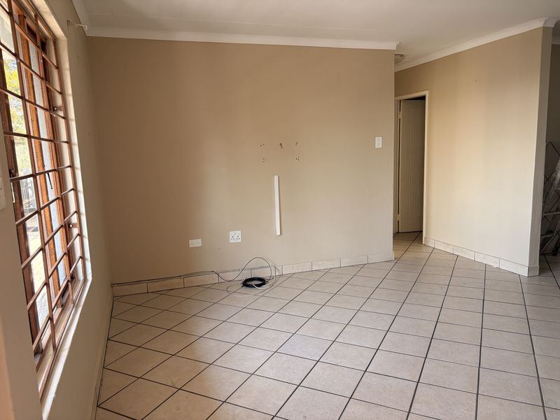 An empty living area featuring tiled flooring and security bars on the window, requiring minor wall repairs and cosmetic updates.