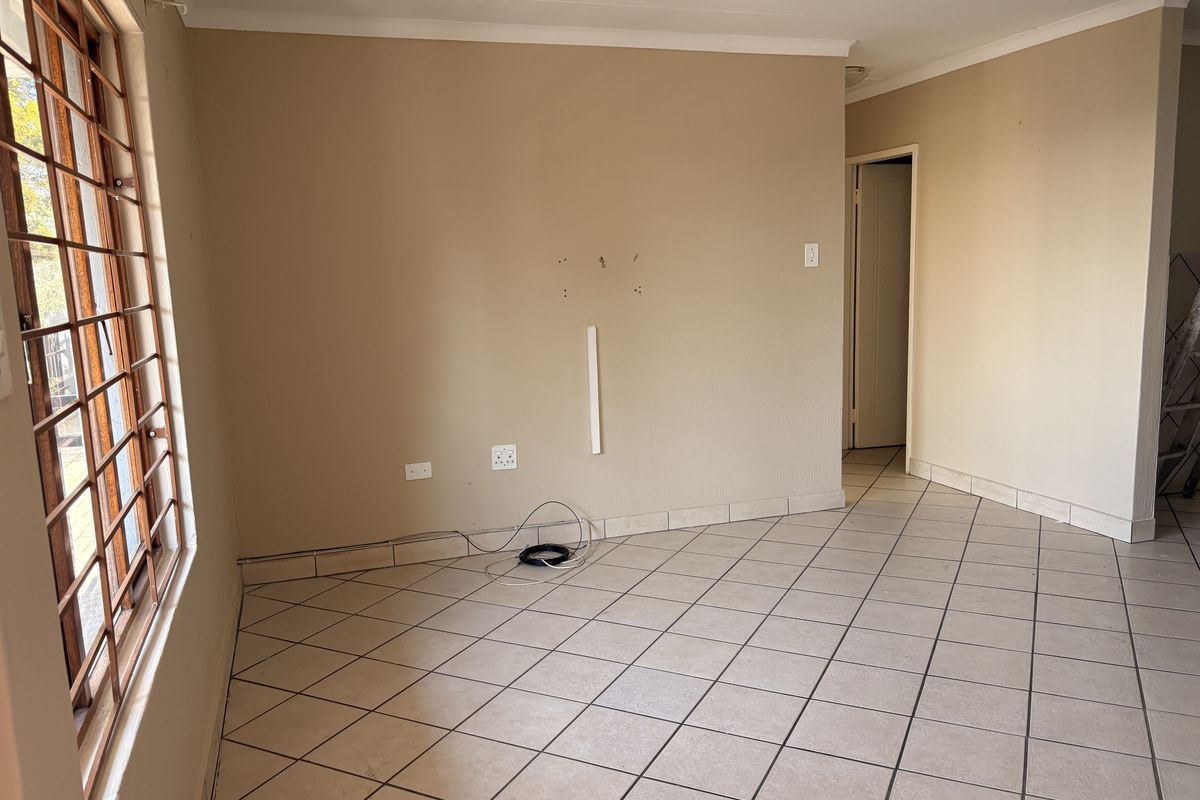 An empty living area featuring tiled flooring and security bars on the window, requiring minor wall repairs and cosmetic updates.