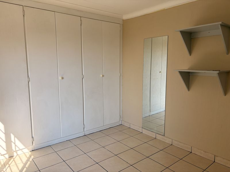 A vacant bedroom featuring built-in cupboards, tiled flooring, and wall-mounted shelving, offering a neutral canvas for personalization.