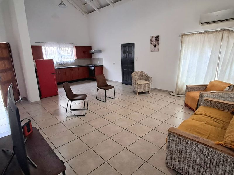 Spacious open-plan living area featuring tiled floors, vaulted ceilings with exposed rafters, and a functional kitchen with built-in cabinetry.