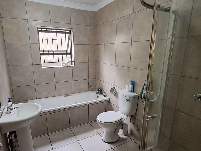 A functional bathroom featuring a pedestal basin, built-in bathtub, toilet, and a corner shower enclosure with tiled finishes throughout.