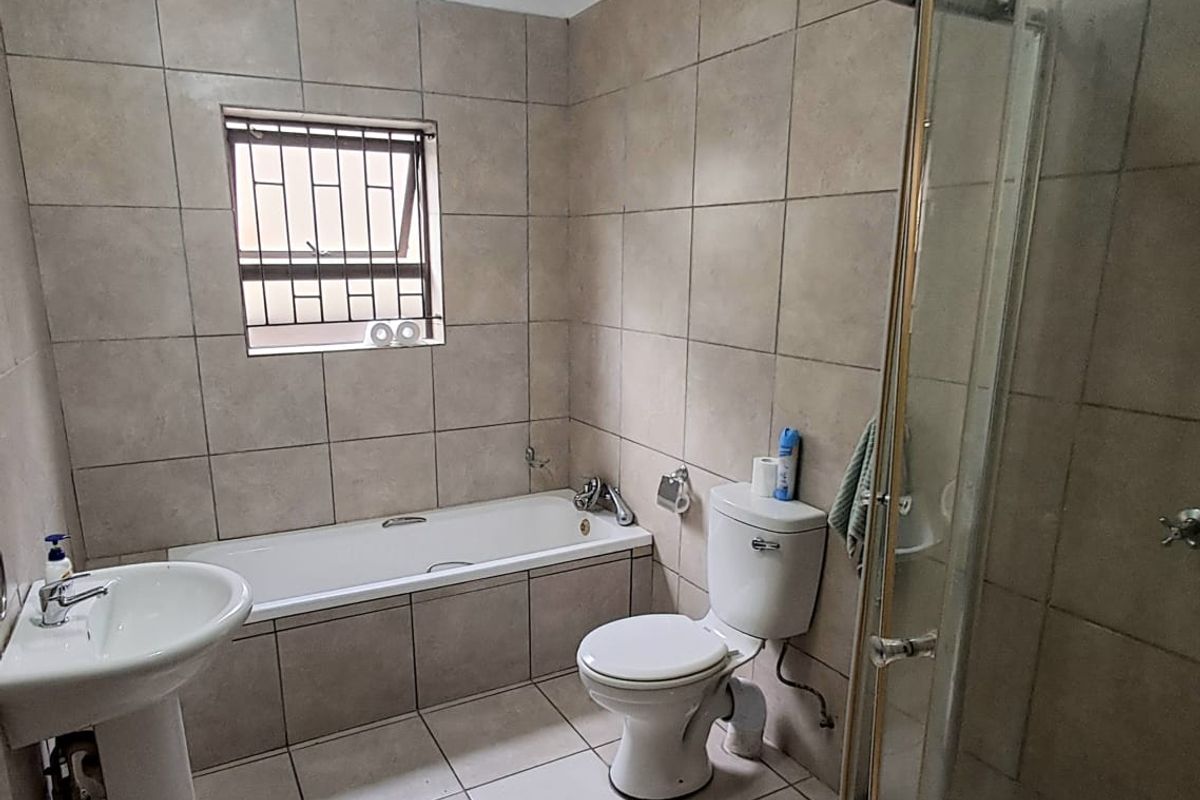 A functional bathroom featuring a pedestal basin, built-in bathtub, toilet, and a corner shower enclosure with tiled finishes throughout.