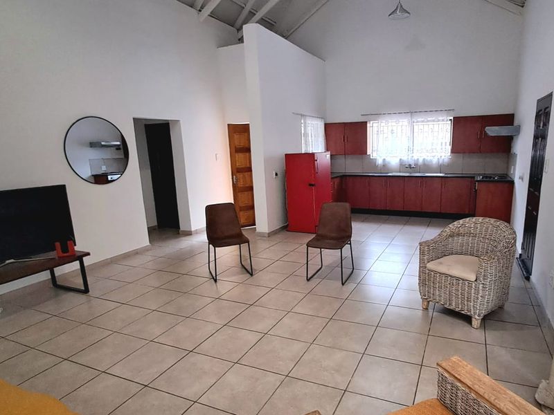 Spacious open-plan living and kitchen area featuring vaulted ceilings, tiled flooring, and functional kitchen cabinetry with integrated appliances.