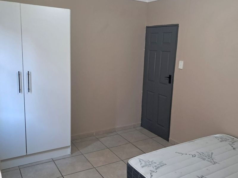 A simple bedroom featuring neutral wall tones, tiled flooring, and a built-in wardrobe, offering a clean and functional space ready for personalization.