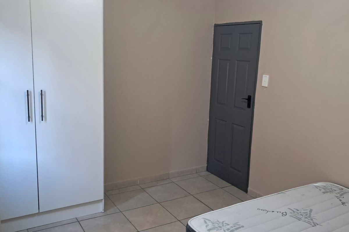 A simple bedroom featuring neutral wall tones, tiled flooring, and a built-in wardrobe, offering a clean and functional space ready for personalization.