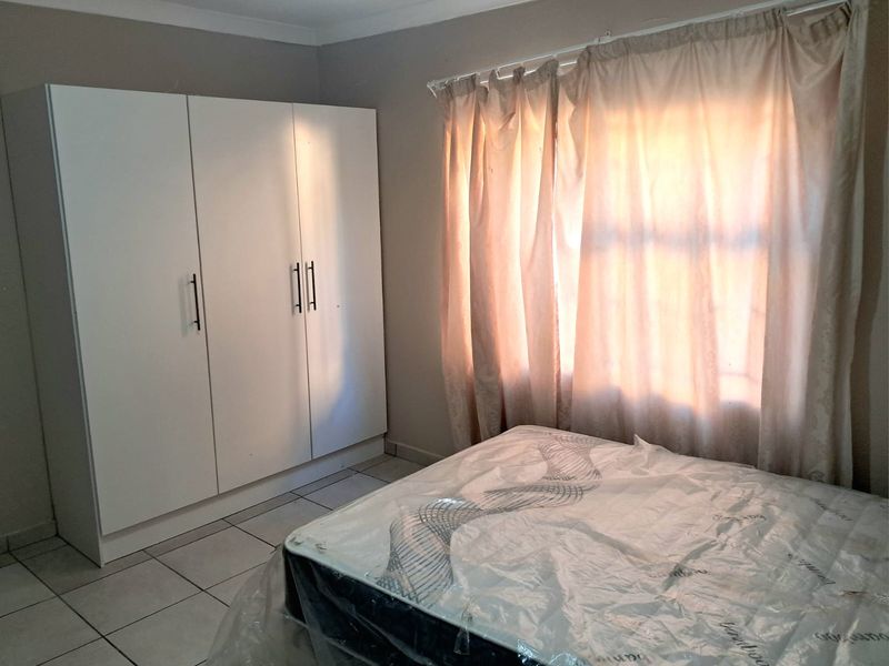 A functional bedroom featuring tiled flooring, a built-in wardrobe, and natural light through the window.