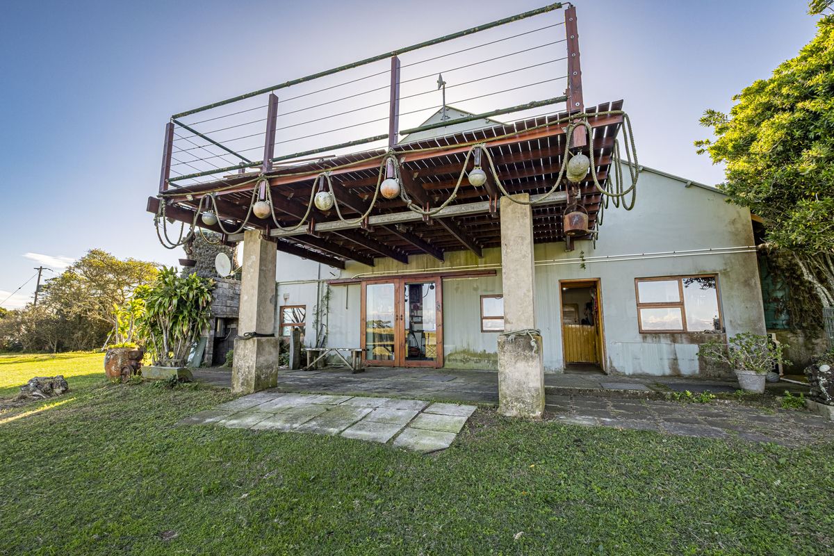 Rear view of the property featuring a raised timber deck with cable balustrade, concrete patio area, and sliding glass door access to the main dwelling.