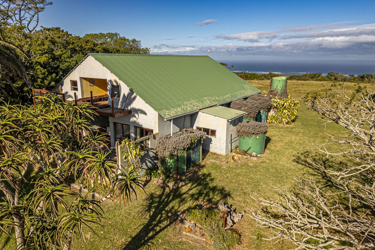 Aerial view of a rural small holding property featuring a pitched metal roof, water storage tanks, and a wooden balcony overlooking the landscape.