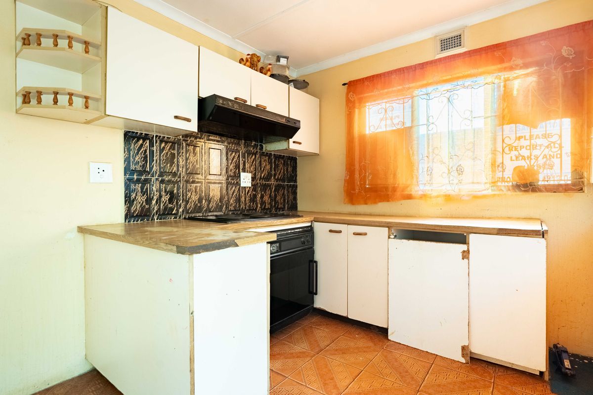 A compact kitchen featuring built-in cabinetry, a fitted oven and hob, extractor fan, and tiled flooring, requiring cosmetic updates.