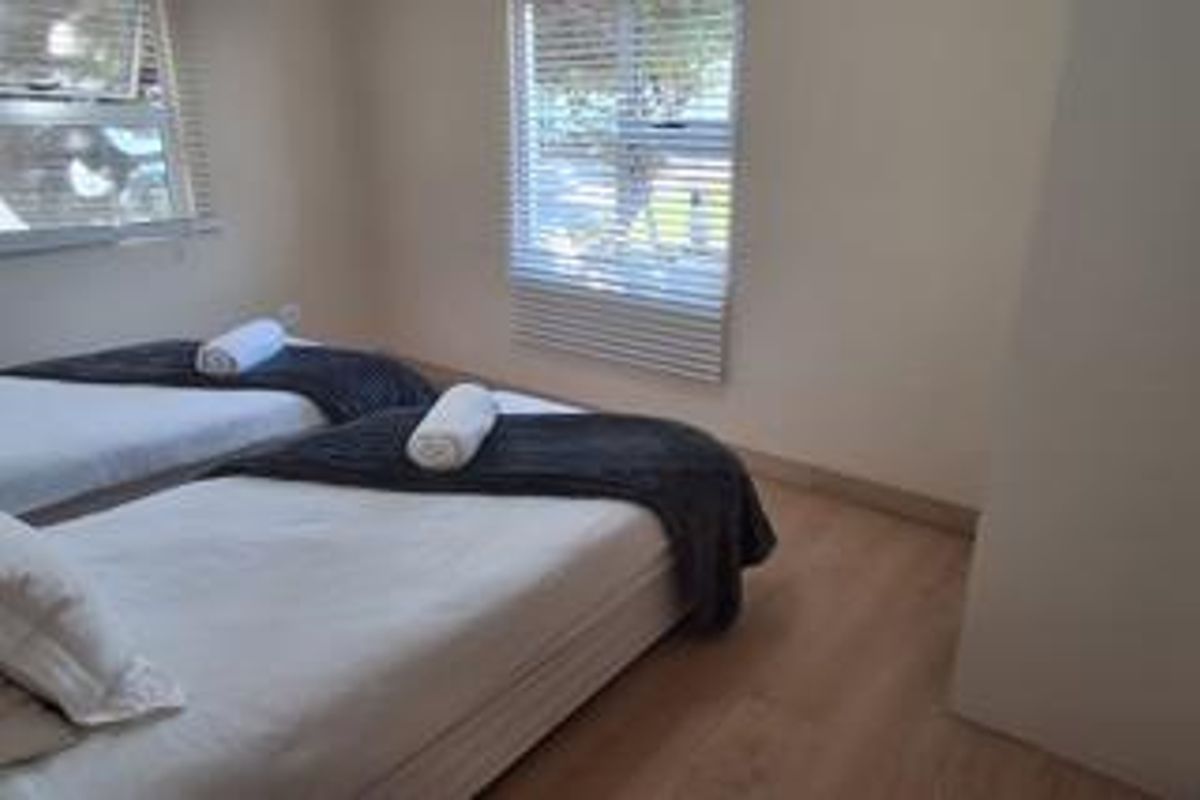 A bedroom featuring light-toned laminate flooring and venetian blinds on the windows, providing a neutral and functional space.