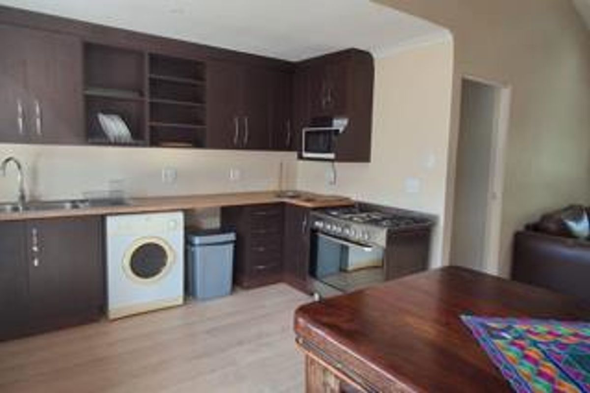 A functional kitchen featuring dark wood cabinetry, laminate countertops, a gas stove, and built-in microwave, with integrated space for laundry appliances.