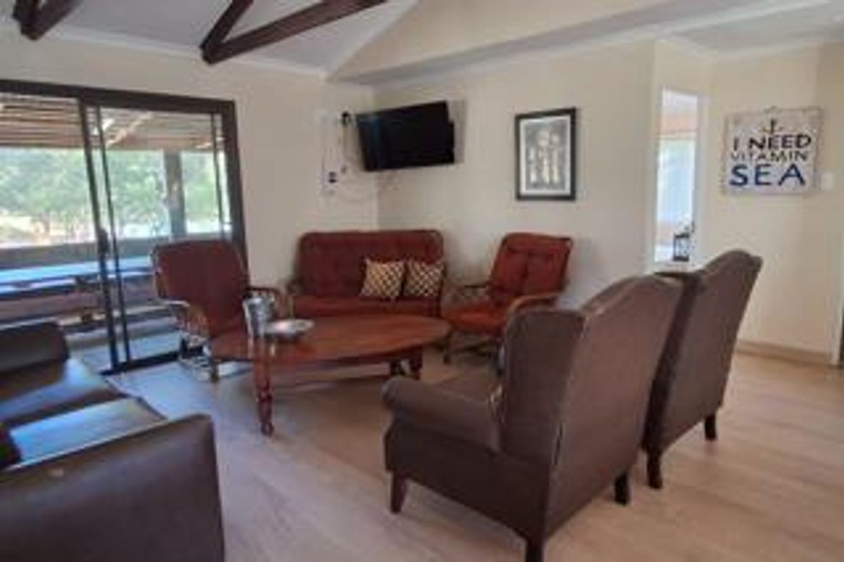 A living room featuring exposed timber ceiling beams, light laminate flooring, and a sliding glass door providing access to the outdoor patio area.