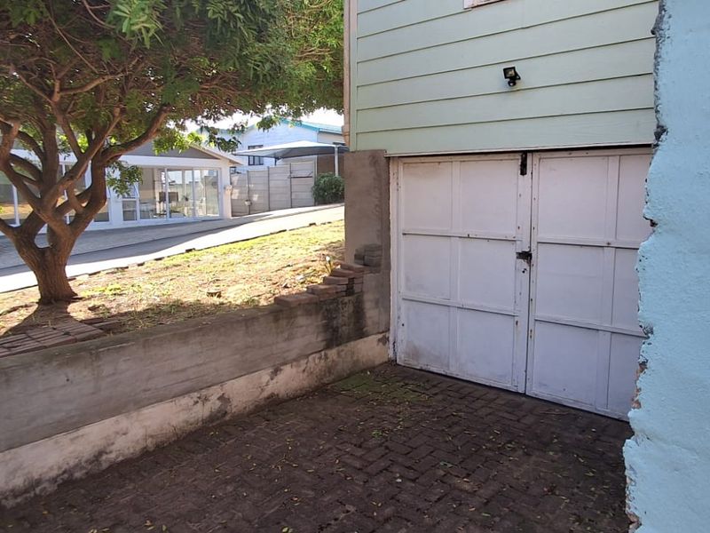 Exterior view of a garage with double swing doors, featuring a paved driveway and a concrete retaining wall with visible masonry damage.