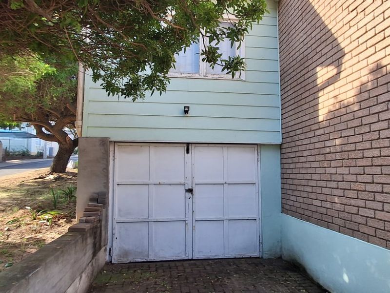 Exterior view of a garage featuring double doors, brickwork, and weatherboard cladding, situated alongside a paved driveway area.