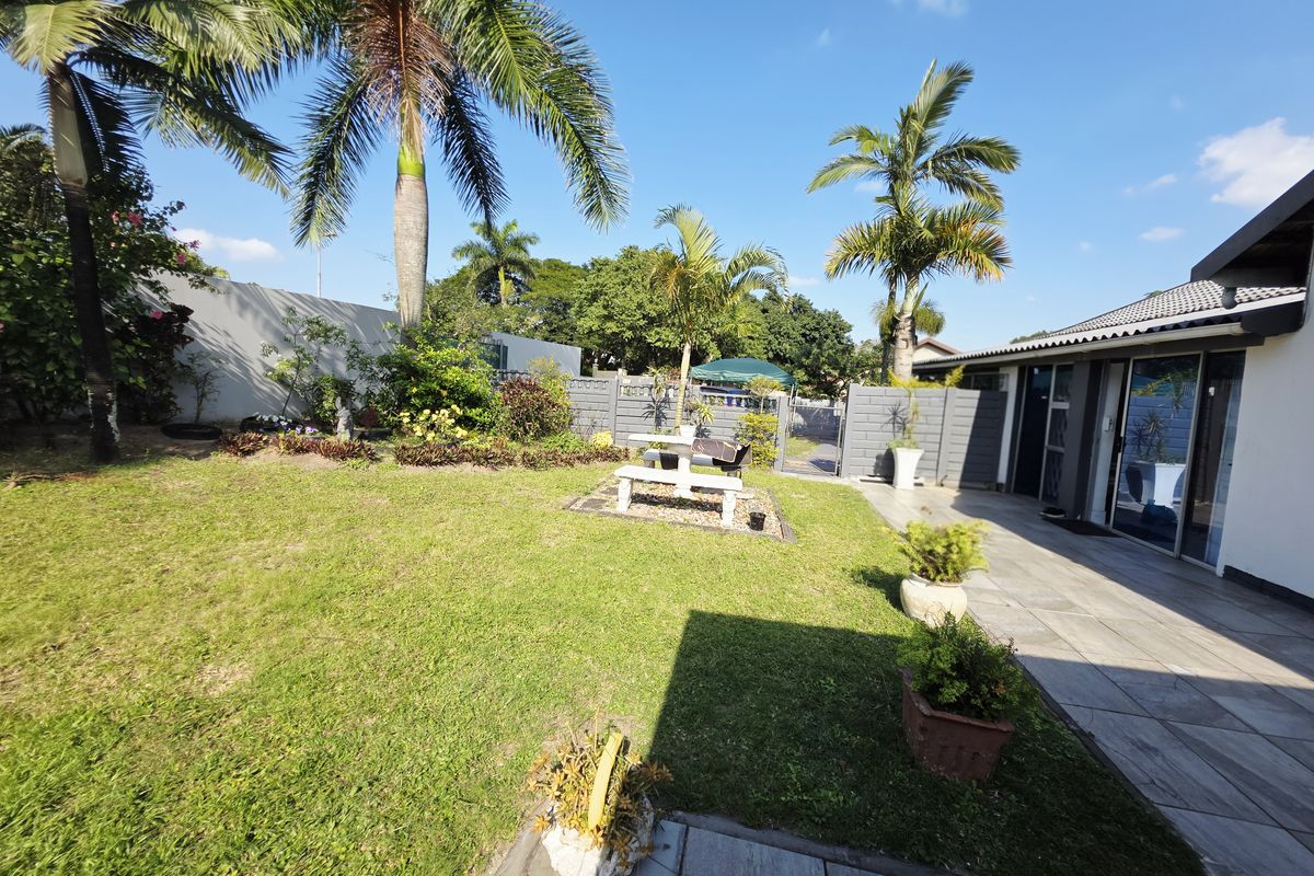 A well-maintained rear garden featuring a tiled patio area, lush lawn, and established palm trees, providing a pleasant outdoor space.