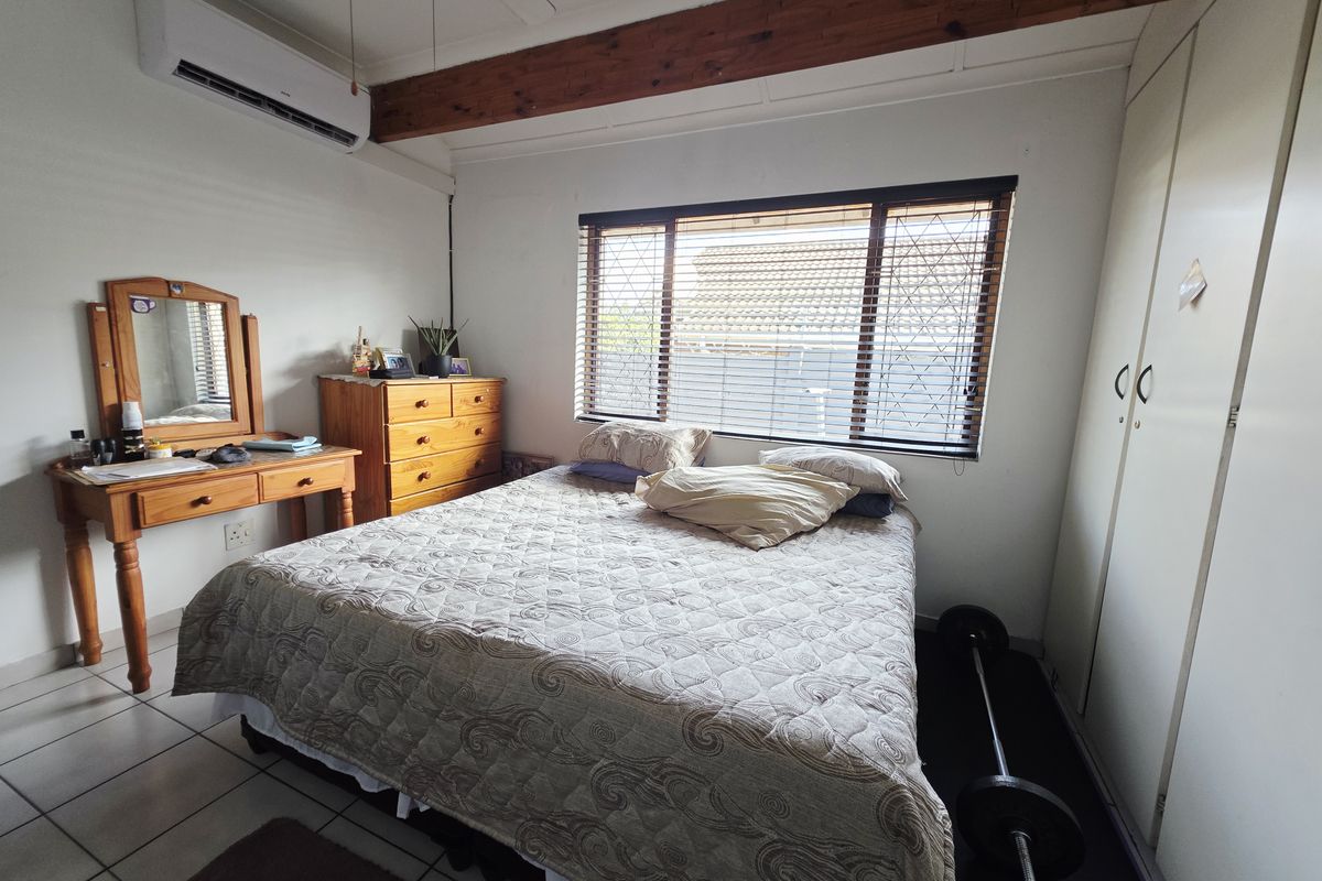 A functional bedroom featuring tiled flooring, built-in cupboards, an exposed timber ceiling beam, and a wall-mounted air conditioning unit.