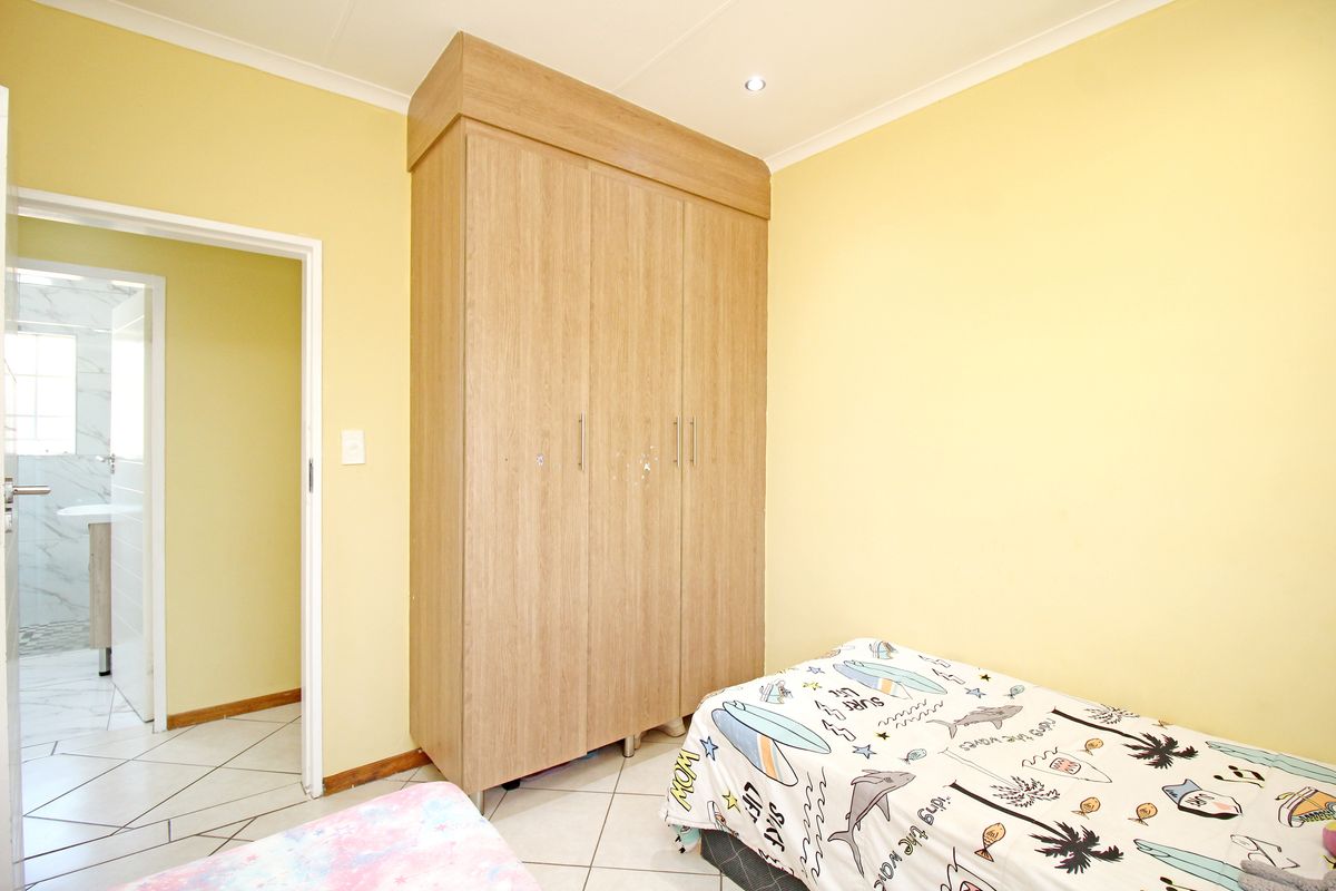 A bedroom featuring built-in wooden cabinetry and tiled flooring, with an adjacent view into a tiled bathroom.