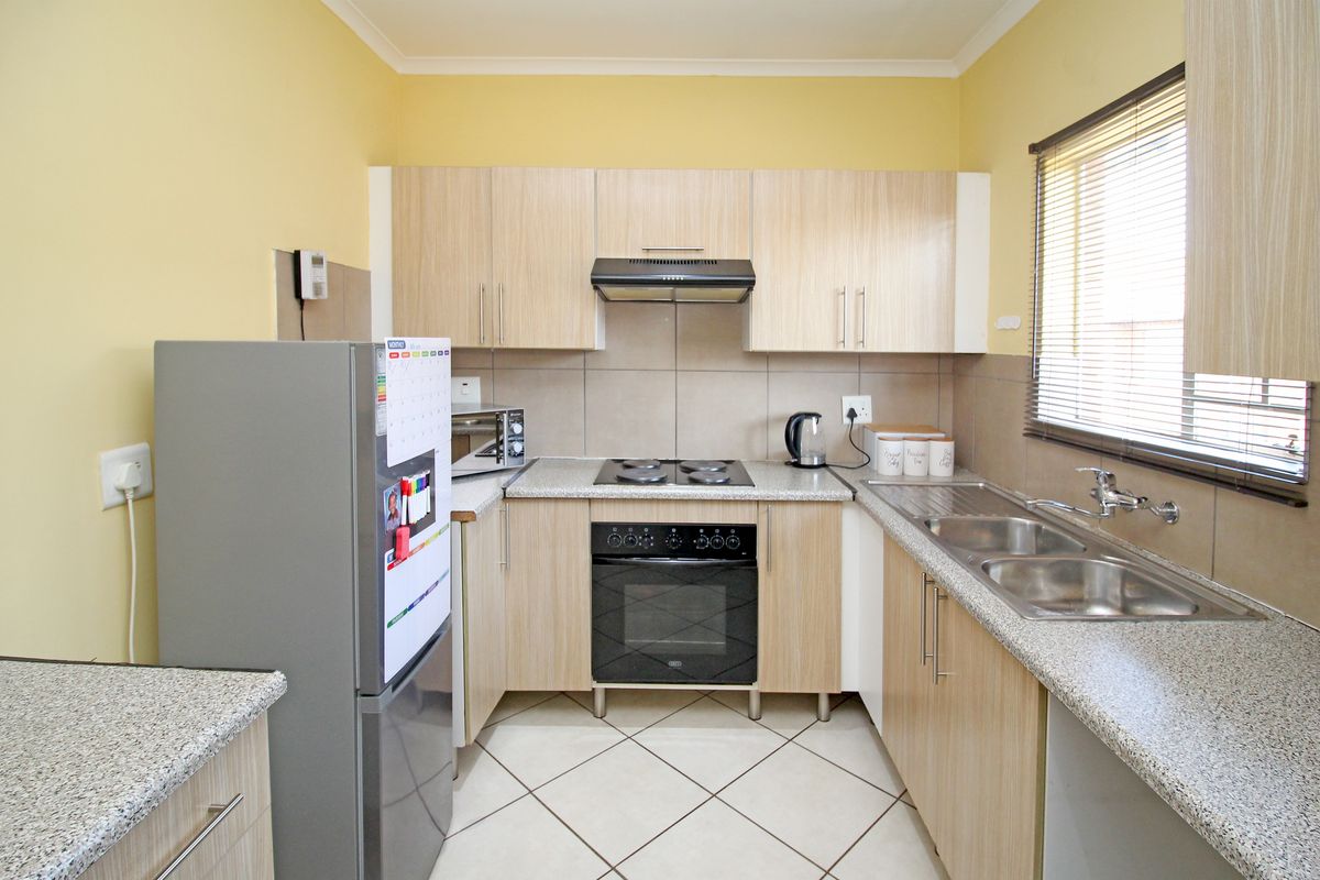 A functional kitchen featuring light wood-finish cabinetry, granite-look countertops, a built-in oven with hob, extractor fan, and a double stainless steel sink.
