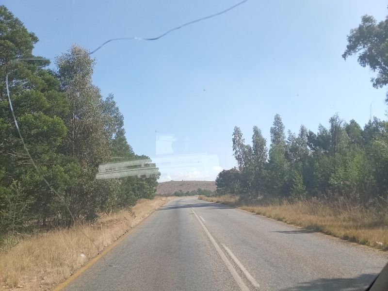 A view of a paved road leading towards a distant hill, captured from inside a vehicle.
