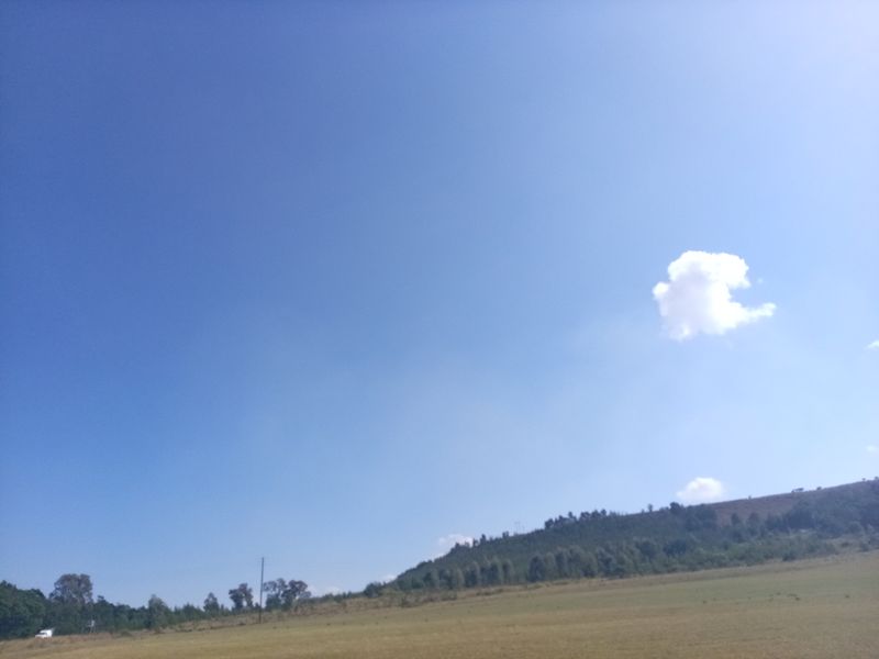 A wide-angle view of the vacant residential land featuring open grassy terrain and distant hillside landscape under a clear blue sky.