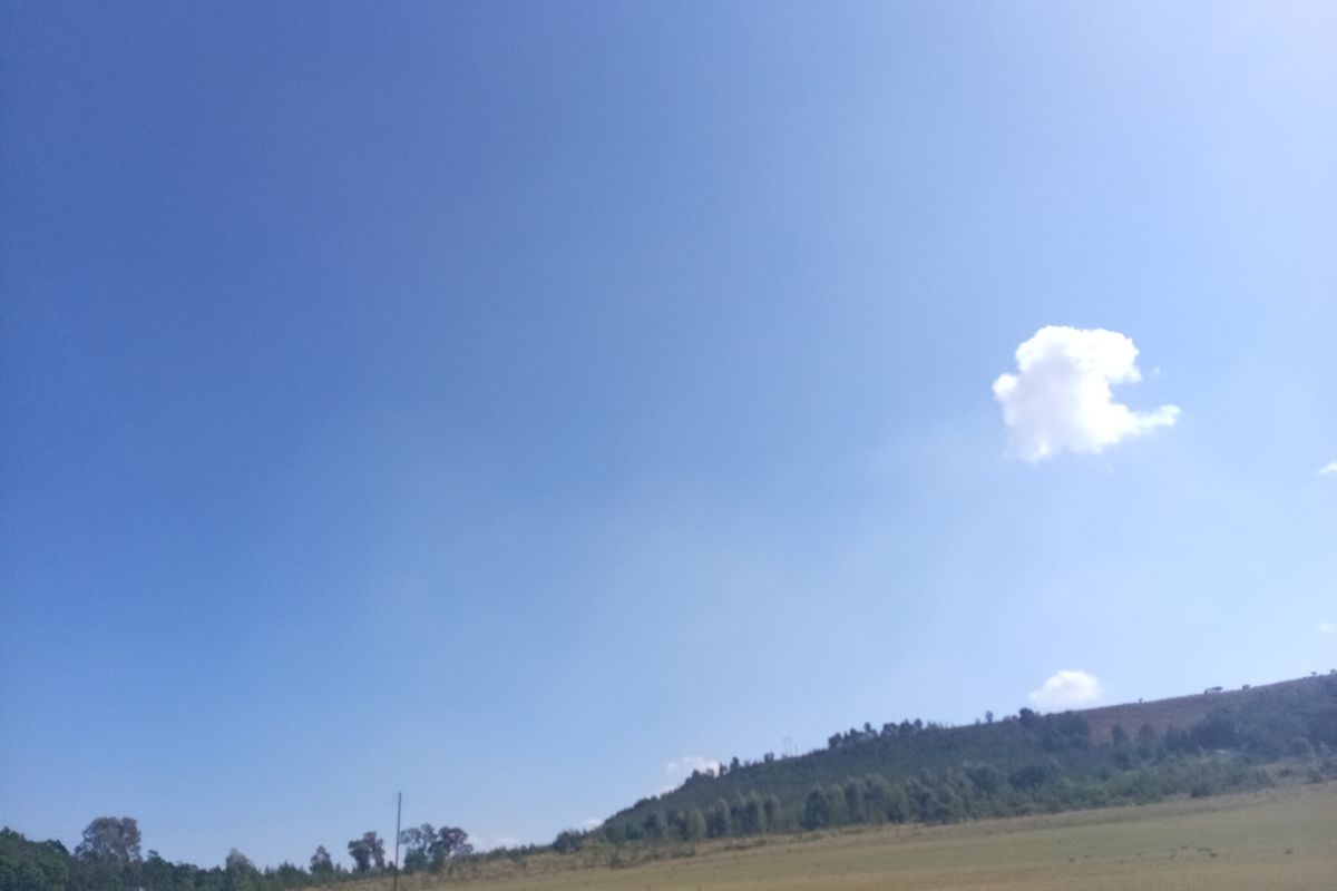 A wide-angle view of the vacant residential land featuring open grassy terrain and distant hillside landscape under a clear blue sky.