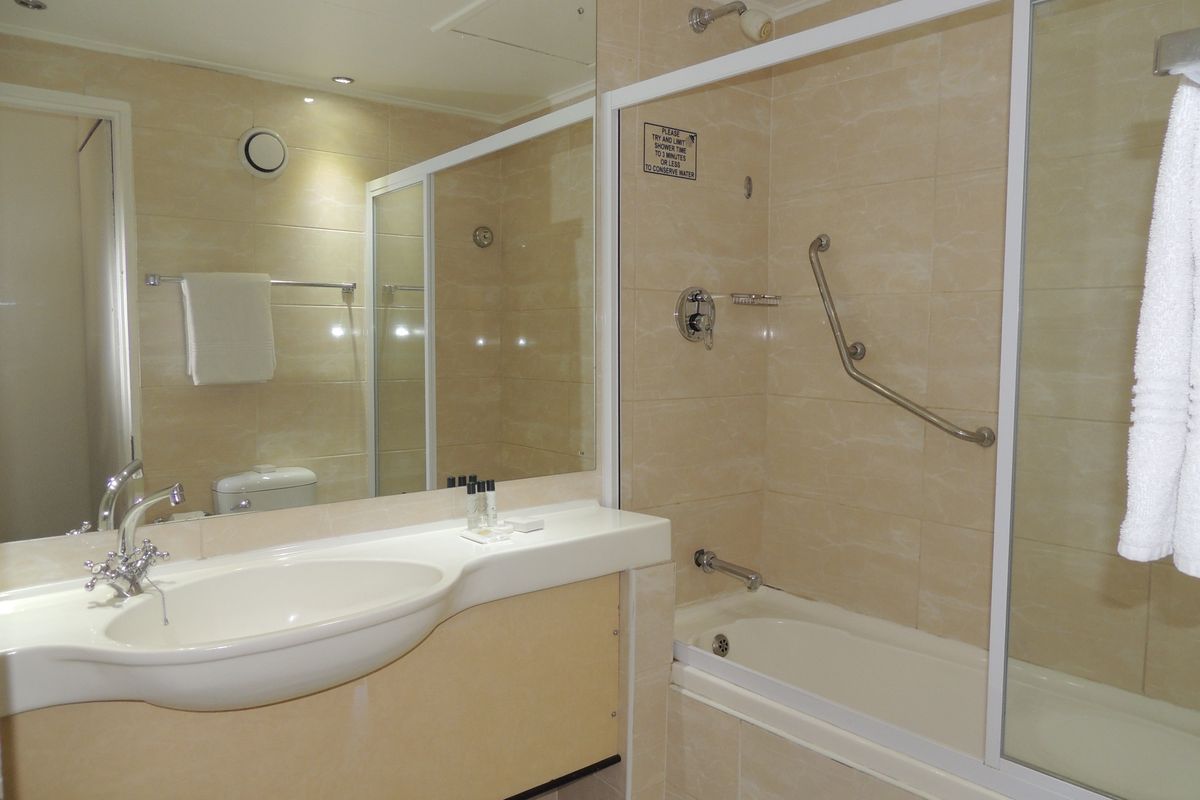 A functional bathroom featuring a built-in vanity with integrated sink, a bathtub with shower combination, and neutral wall tiling.