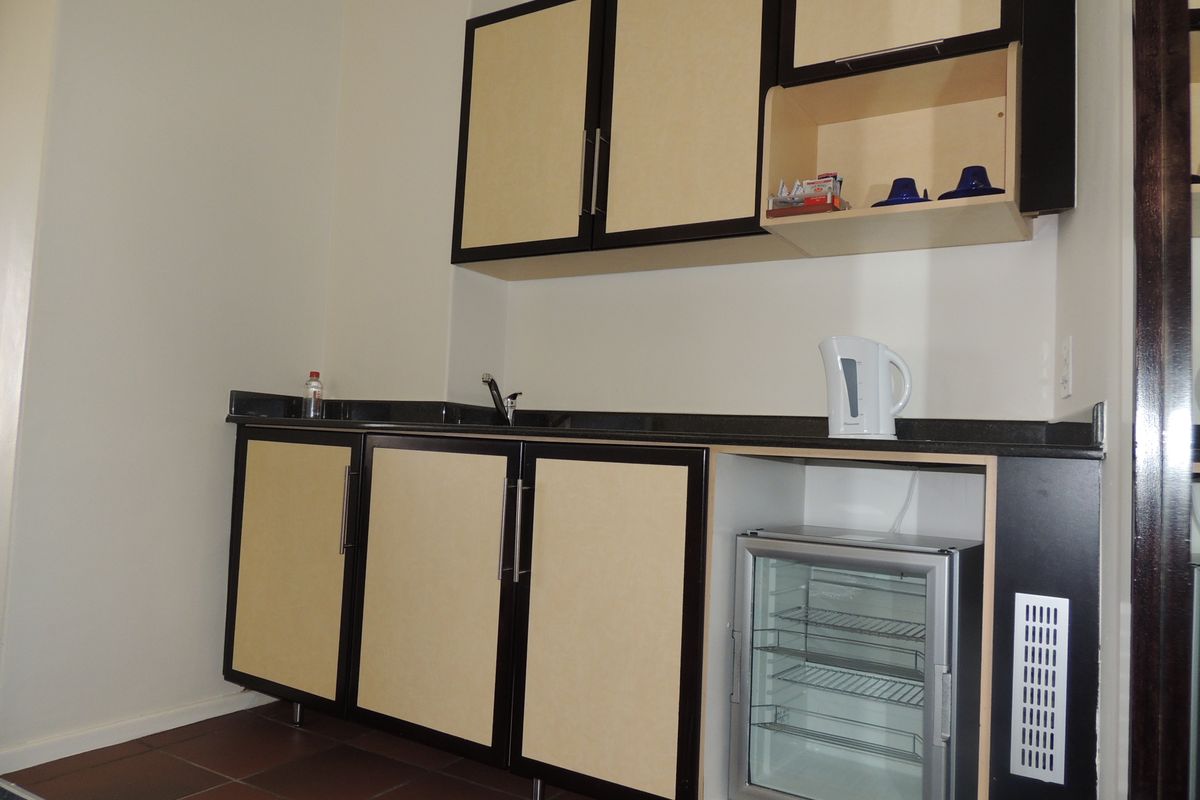 A compact kitchenette featuring built-in cabinetry, a dark granite countertop, an undermount sink, and tiled flooring.