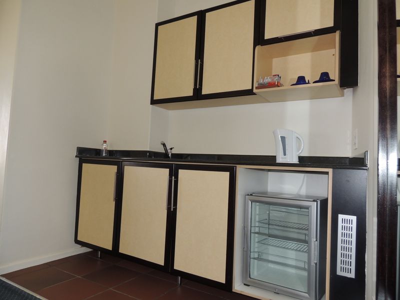 A compact kitchenette featuring built-in cabinetry, a dark granite countertop, an undermount sink, and tiled flooring.