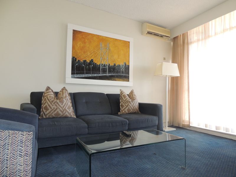 A living room featuring carpeted flooring, a wall-mounted air conditioning unit, and a large window allowing natural light.
