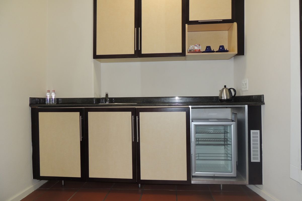 A compact kitchenette featuring built-in cabinetry, granite countertops, an integrated bar fridge, and durable tiled flooring.