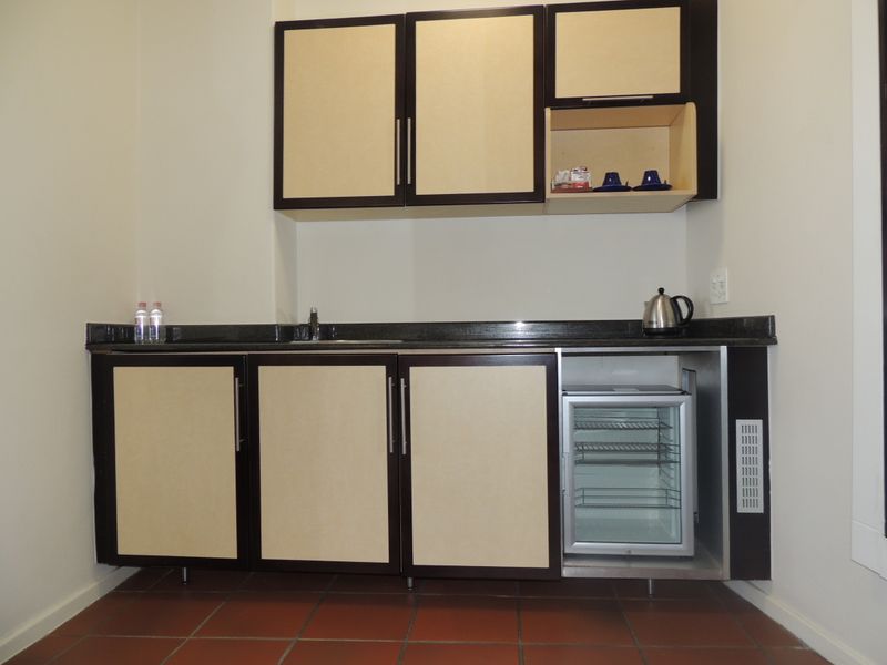 A compact kitchenette featuring built-in cabinetry, granite countertops, an integrated bar fridge, and durable tiled flooring.