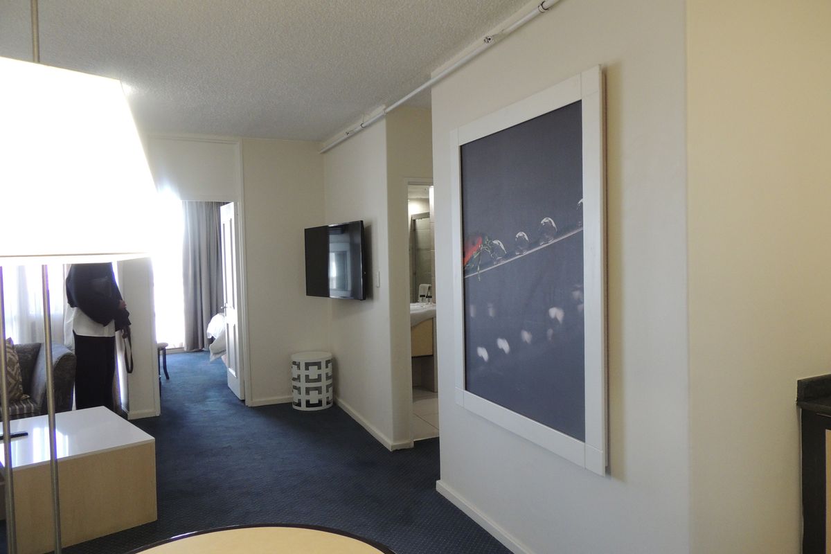 A living area featuring carpeted flooring, a wall-mounted television, and access to adjacent rooms, showing a standard, functional layout.
