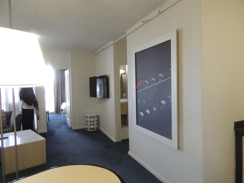 A living area featuring carpeted flooring, a wall-mounted television, and access to adjacent rooms, showing a standard, functional layout.