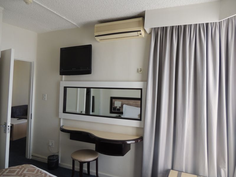 A bedroom featuring a built-in vanity with an integrated mirror and a wall-mounted air conditioning unit, showing signs of age and wear.