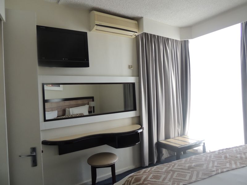 A bedroom featuring a built-in vanity desk, wall-mounted mirror, and air conditioning unit, with floor-to-ceiling curtains providing access to natural light.