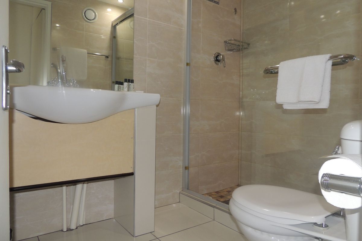 A functional bathroom featuring a glass-enclosed shower, wall-mounted basin, and tiled finishes throughout.