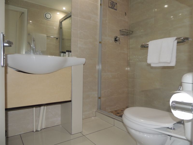 A functional bathroom featuring a glass-enclosed shower, wall-mounted basin, and tiled finishes throughout.